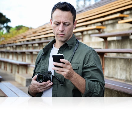 Photo of a man with the Nikon 1 V3 in his hand, looking at an image in his smartphone